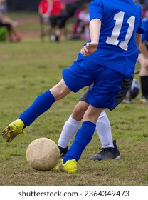 A young boy wearing a blue jersey is kicking a soccer ball on a soccer field - Shutterstock ID 2364349473