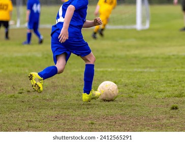 A young boy wearing a blue jersey is kicking a soccer ball on a soccer field - Powered by Shutterstock