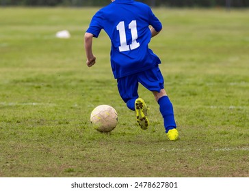 A young boy wearing a blue jersey is kicking a soccer ball on a soccer field - Powered by Shutterstock