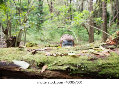 Young Boy Wearing Camouflage Face Paint Plays Soldier While Hiding Among Trees And Logs In The Forest.  Oahu, Hawaii.