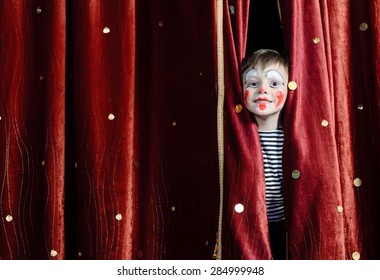 Young Boy Wearing Clown Make Up Peering Out Through Opening in Red Stage Curtains