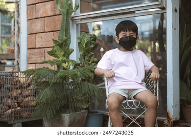 Young boy wearing a mask, sitting outside next to plants. - Powered by Shutterstock