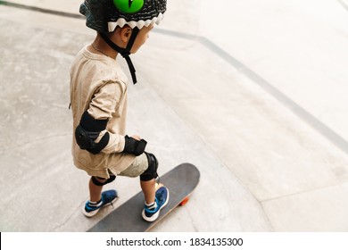 Young Boy Wearing Safety Gear At The Skateboard Park, Back View