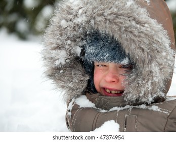 Young boy wearing winter jacket with furry hood playing in snow
