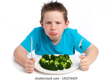 A young boy who is not happy about eating his broccoli. Isolated on white background.