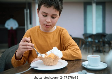 Young boy in a yellow shirt relishing an ice cream sundae with whipped cream at an outdoor cafe. Relaxing and enjoying a sweet treat. - Powered by Shutterstock