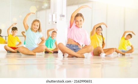 Young Boys And Girls Training Together During Group Ballet Class. They're Doing Exercises While Sitting On Floor.