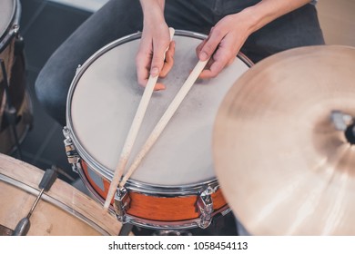 Young boy's hands holding wooden drum sticks on red vintage drums, snare, hi-hat, bass drum in the house with stripped colorful carpet