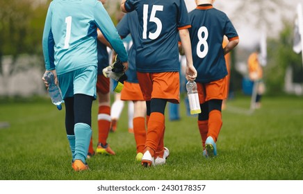 Young boys in the sports team walk off the grass pitch holding bottles of water in their hands after losing the game. Kids in blue soccer jerseys. Male elementary school sports team - Powered by Shutterstock