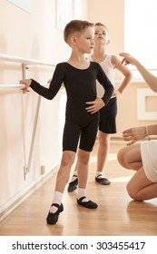 Young boys working at the barre in a ballet dance class. Teacher adjusting the position of one of them.