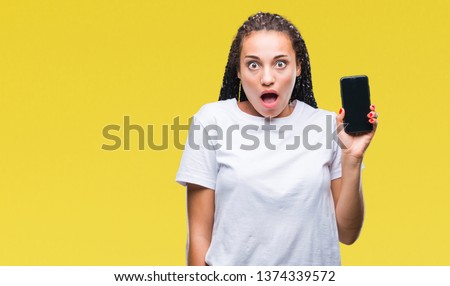 Young braided hair african american girl showing screen of smartphone over isolated background scared in shock with a surprise face, afraid and excited with fear expression