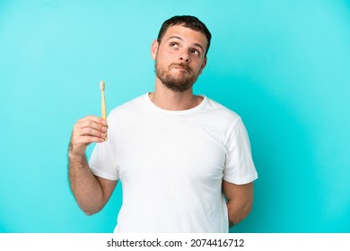Young Brazilian man brushing teeth isolated on blue background and looking up