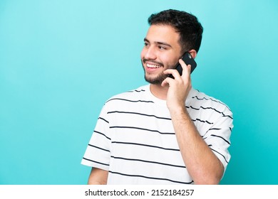 Young Brazilian Man Isolated On Blue Background Keeping A Conversation With The Mobile Phone With Someone