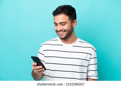 Young Brazilian man isolated on blue background sending a message or email with the mobile