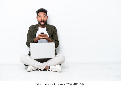 Young Brazilian man with a laptop sitting on the floor isolated on white surprised and sending a message - Shutterstock ID 2190481787