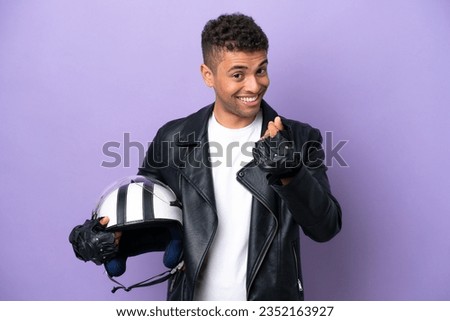 Young Brazilian man with a motorcycle helmet isolated on purple background making money gesture
