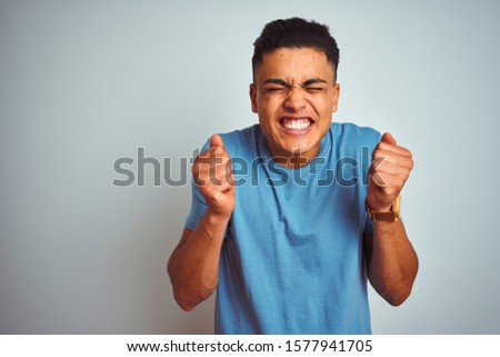 Young brazilian man wearing blue t-shirt standing over isolated white background excited for success with arms raised and eyes closed celebrating victory smiling. Winner concept.