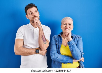 Young brazilian mother and son standing over blue background with hand on chin thinking about question, pensive expression. smiling and thoughtful face. doubt concept.  - Shutterstock ID 2230644317