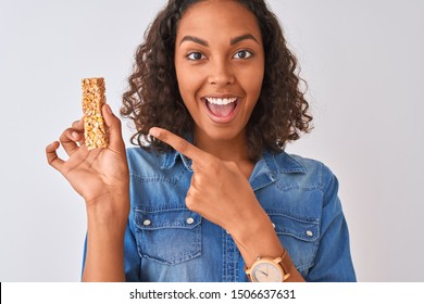 Young Brazilian Woman Eating Granola Bar Standing Over Isolated White Background Very Happy Pointing With Hand And Finger