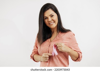 Young Brazilian woman holding breast cancer ribbon over white background - Shutterstock ID 2203973043