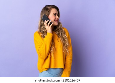 Young Brazilian woman isolated on purple background keeping a conversation with the mobile phone with someone