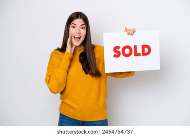 Young Brazilian woman isolated on white background holding a placard with text SOLD and shouting - Powered by Shutterstock