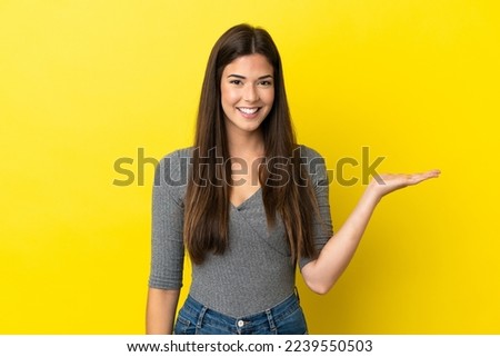 Young Brazilian woman isolated on yellow background holding copyspace imaginary on the palm to insert an ad
