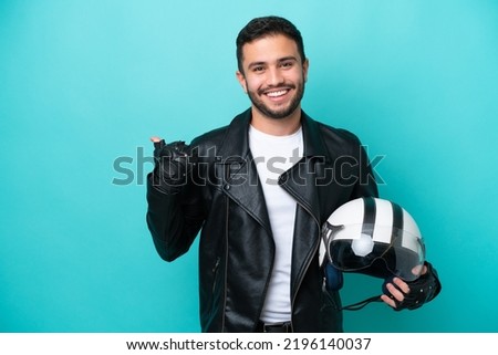 Young Brazilian woman with a motorcycle helmet isolated on blue background pointing to the side to present a product