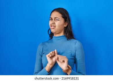 Young brazilian woman standing over blue isolated background disgusted expression, displeased and fearful doing disgust face because aversion reaction. 