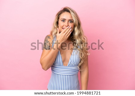 Young Brazilian woman in swimsuit in summer holidays isolated on pink background happy and smiling covering mouth with hand