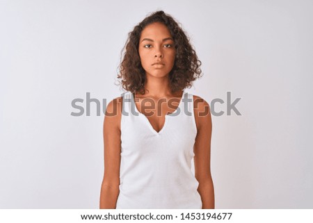 Young brazilian woman wearing casual t-shirt standing over isolated white background with serious expression on face. Simple and natural looking at the camera.