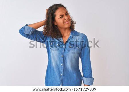 Young brazilian woman wearing denim shirt standing over isolated white background confuse and wondering about question. Uncertain with doubt, thinking with hand on head. Pensive concept.
