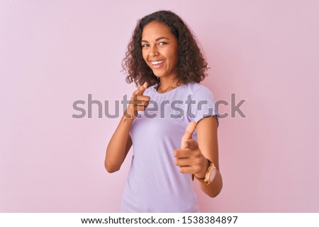 Young brazilian woman wearing t-shirt standing over isolated pink background pointing fingers to camera with happy and funny face. Good energy and vibes.