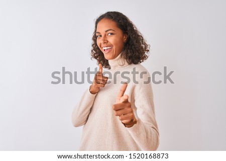 Young brazilian woman wearing turtleneck sweater standing over isolated white background pointing fingers to camera with happy and funny face. Good energy and vibes.