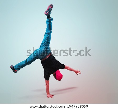 Young breakdancer guy stands on one hand dancing and posing