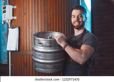 A young brewer in an apron holds a barrel with beer in the hands of a brewery. - Powered by Shutterstock