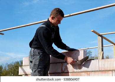 Young Bricklayer Mason Is Building A Wall Under Blue Sky