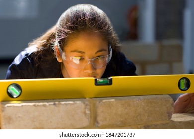 A young Bricklaying student in a vocational school using the spirit level on a brick wall while closely watching the alignment of the bricks - Shutterstock ID 1847201737