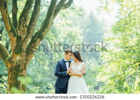 young bride and groom hug and look at each other in a green summer forest