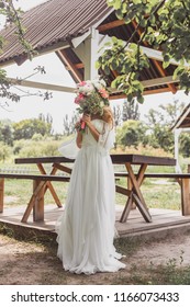 Young Bride Hiding Face With Bouquet Of Flowers Outdoors