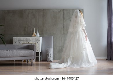 A Young Bride In A Wedding Dress Stands In The Middle Of The Room Alone With Her Back To The Viewer, Waiting.