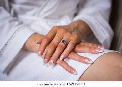 Young bride's hands with white gold sapphire engagement ring on the finger, elegant french manicure, tanned skin, white robe - Shutterstock ID 1762358852