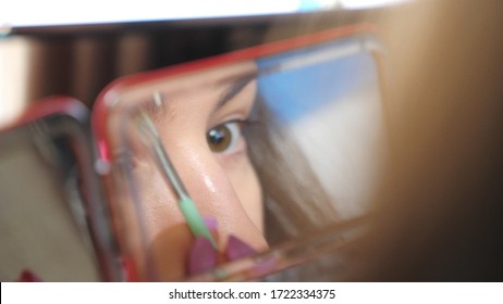 Young brown eyed girl reflect in mirror during applying mascara on eyelashes. Attractive woman taking care of himself doing make up. Concept of fashion and style. Slow motion Detail view.