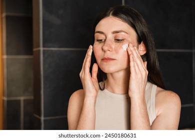 Young brunette applies sunscreen to her face. Skincare routine. Concept of skincare. - Powered by Shutterstock