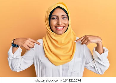Young brunette arab woman wearing traditional islamic hijab scarf looking confident with smile on face, pointing oneself with fingers proud and happy. 
