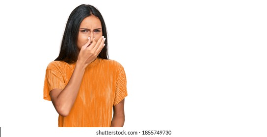 Young Brunette Arab Woman Wearing Casual Clothes Smelling Something Stinky And Disgusting, Intolerable Smell, Holding Breath With Fingers On Nose. Bad Smell 