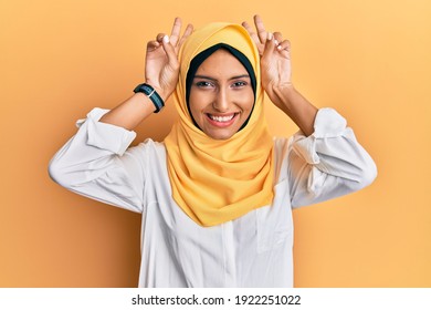 Young brunette arab woman wearing traditional islamic hijab scarf posing funny and crazy with fingers on head as bunny ears, smiling cheerful  - Powered by Shutterstock - Get 15% off with code: PIKWIZARD15