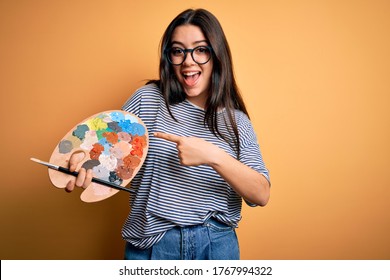 Young Brunette Artist Woman Painting Holding Painter Brush And Palette Over Yellow Background Very Happy Pointing With Hand And Finger