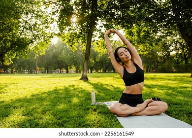 Young brunette asian woman practicing yoga during workout in park - Powered by Shutterstock