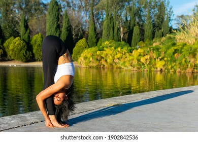 Young brunette attractive sporty girl practicing yoga, doing folding exercise, posed uttanasana, exercising, wearing sportswear and in a lake in the background. Concept of self-love